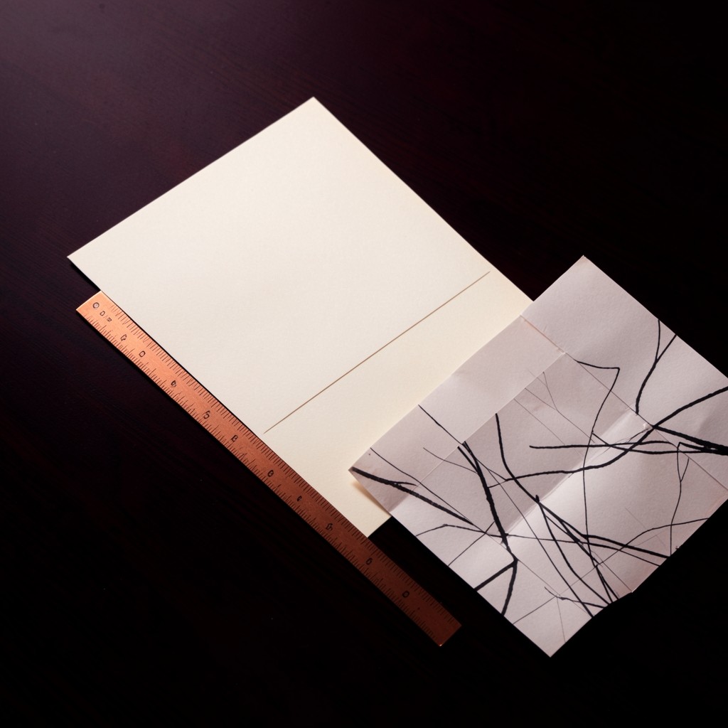A blank ivory card and a copper ruler on dark lacquered wood beside a paper chart